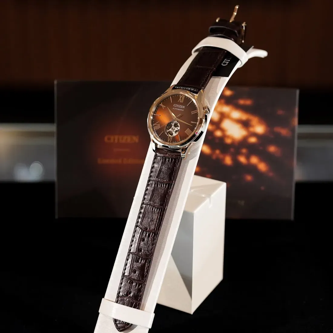 The Citizen watch mounted on a white, curved display stand. The image showcases the full length of the crocodile-embossed dark brown leather strap and - Capped at 300 Pieces, Citizen's Warmest Dial Captures Seasonal Light