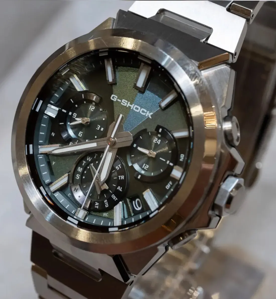 Close-up of the green-dial Casio G-Shock GST-W1000D-3A, showing its geometric textured dial, three subdials, luminous markers, and polished stainless - Casio's Sleeker G-Steel GST-W1000 Swaps Rugged Bulk for Refined Steel