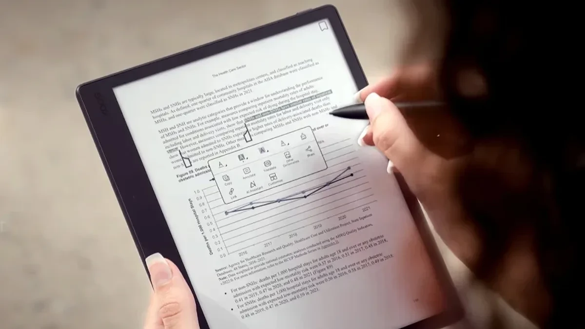 The Boox Note Mini C held in one hand, displaying a colorful document with the stylus resting nearby.